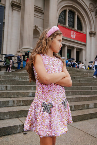 Lola and The Boys Rosie Bows Dress Young girl in a floral dress standing on steps in front of a large building with a red sign.
