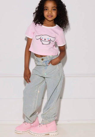 Lola and The Boys Sparkle Crystal Denim Jeans
A young girl with curly black hair stands against a white paneled wall wearing a light pink cropped t-shirt with a cartoon dog graphic, light blue sparkly denim jeans, and pink high-top sneakers.