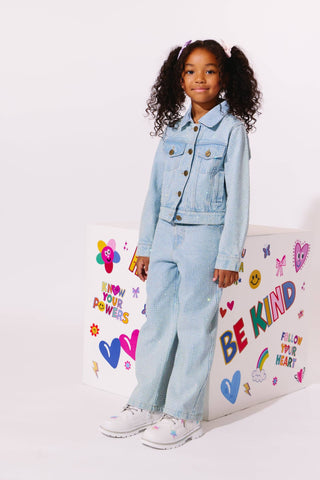 Lola and The Boys Sparkle Crystal Denim Jeans
A young girl with curly hair stands in a studio wearing a light blue denim jacket and matching wide-leg jeans, paired with white sneakers. She is posed next to a white decorative box with colorful text and heart graphics.
