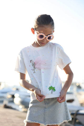 Lola and The Boys Sparkle Flamingo T-shirt Person wearing a white t-shirt with palm tree design and denim skirt outdoors.