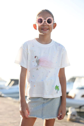 Lola and The Boys Sparkle Flamingo T-shirt
Child wearing a white t-shirt with colorful designs and a denim skirt, standing outdoors.