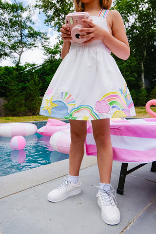 Lola and The Boys Summer Pop Dress
Child wearing a white dress with rainbow designs by a poolside.