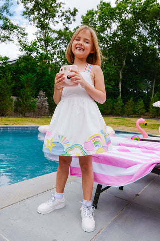 Lola and The Boys Summer Pop Dress
Young girl in a white dress with colorful accents standing by a pool holding a phone.