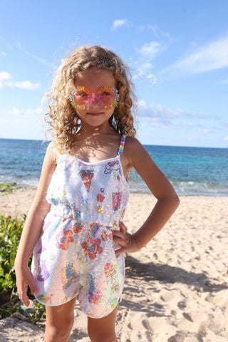 Lola and The Boys Summertime Fun Sequin Romper
Young girl in a floral dress standing on a beach with ocean in the background