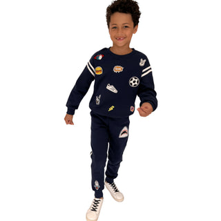 Lola and The Boys Varsity Patch Jogger Set - Navy
A young boy modeling a navy blue two-piece tracksuit with various colorful sports-themed patches, set against a plain white background.