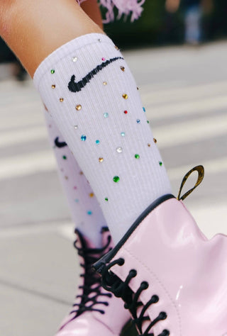 Lola and the Boys Gem Athletic Socks - White
White socks with colorful embellishments and a black logo worn with pink shoes on a blurred background.