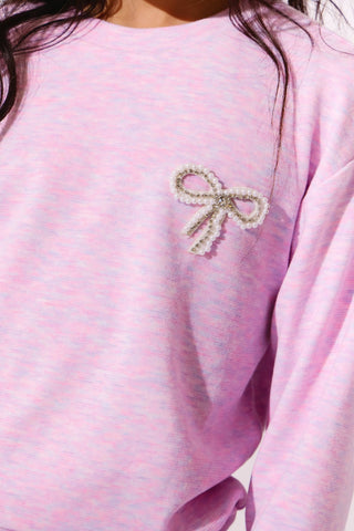 Lola and the Boys Super Soft Pearl Bow Set - Lavender
A close-up of a person wearing a light pink long-sleeve top with a decorative pearl bow embellishment on the left chest.