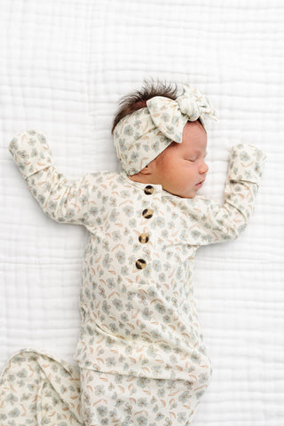 Lou Lou and Company Headband - Faye
A sleeping newborn baby wearing a cream-colored long-sleeve button-front romper and matching bow headband, both with a delicate floral pattern, lying on a white textured blanket.