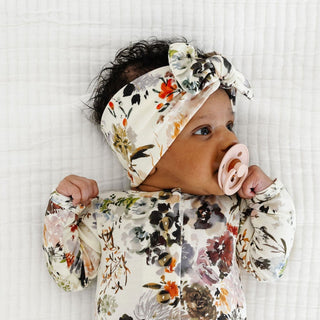 Lou Lou and Company Headband - Nellie
A baby lying on a white textured blanket, wearing a matching floral print onesie and bow headband, with a pink pacifier in their mouth.