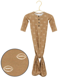 Lou Lou and Company Knotted Gown - Brady
A baby footed sleeper in a tan color with a repeating football pattern, hanging on a gold hanger against a white background, with a circular inset showing a close-up of the fabric pattern.