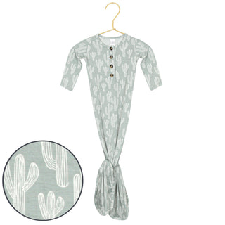 Lou Lou and Company Knotted Gown - Knox
A baby footed sleeper in sage green with a white cactus pattern, hanging on a gold hanger against a white background, with a circular inset showing a close-up of the cactus pattern.