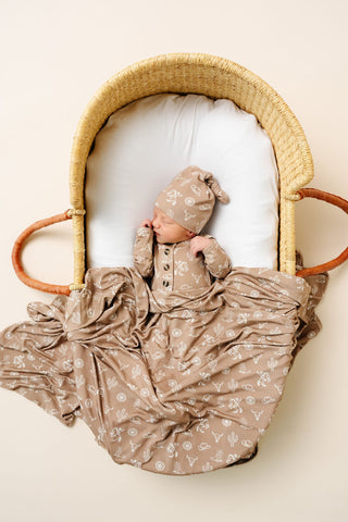 Lou Lou and Company Knotted Gown - Wyatt
Newborn baby in a floral outfit and hat lying in a woven basket on a beige background