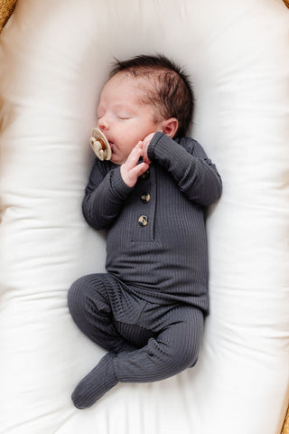 Lou Lou and Company Ribbed Top and Bottoms - Hudson
Newborn baby in a gray outfit with a pacifier, lying on a white cushion.
