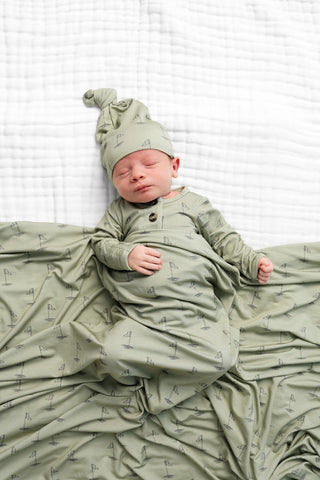 Lou Lou and Company Swaddle Blanket - Cal
Newborn baby in a green outfit and hat lying on a white blanket