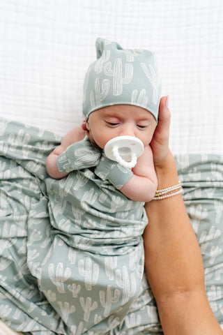 Lou Lou and Company Swaddle Blanket - Knox
Newborn baby wrapped in a green swaddle with matching hat and gloves, held by an adult.