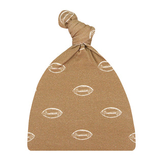 A tan knit baby bonnet with a knotted top Lou Lou and Company Top Knot Hat - Brady
and an allover white football print, shown against a plain white background.