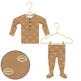 Lou Lou and Company Top and Bottoms - Brady
A baby long-sleeve henley shirt and matching footed pajama pants in tan, both printed with a repeating football pattern. The shirt has a partial button placket.