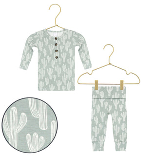 Lou Lou and Company Top and Bottoms - Knox
A two-piece baby clothing set featuring a long-sleeve henley top and matching pants in sage green with a white cactus pattern, shown on hangers with a circular fabric detail inset.
