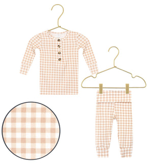 Lou Lou and Company Top and Bottoms - Milo
A baby two-piece outfit set featuring a long-sleeve henley top and matching pants in a light peach and white gingham check pattern, displayed on gold-colored hangers with a circular detail inset of the fabric pattern.