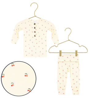 Lou Lou and Company Top and Bottoms - Sadie
A baby pajama set consisting of a long-sleeve henley top and matching pants in a cream color with a small red cherry print, shown on hangers with a circular detail inset of the fabric pattern.