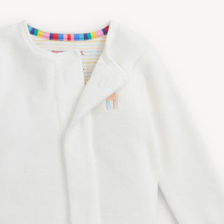 Magnetic Me Embroidery Cream Velour Footie - Giraffe
A close-up of a white baby cardigan or wrap jacket with a soft plush texture, featuring a colorful striped inner collar and a small embroidered llama detail on the chest.