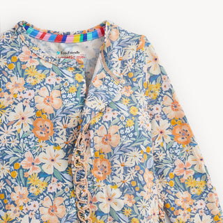 Magnetic Me Modal Footie with Ruffle - Flora
A close-up of a children's long-sleeve top with a blue base and a colorful floral print. The fabric features white, yellow, and orange flowers with green leaves, accented by a ruffled trim down the front.