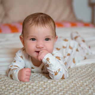 Magnetic Me Modal Magnetic Footie - Wildly Loved 
Baby lying on a bed wearing a white onesie with brown animal patterns.