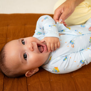 Magnetic Me Modal Magnetic Footie - You Haul
Baby lying on a wooden floor wearing a light blue onesie with colorful patterns.