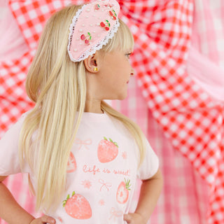 Model wearing Sweet Wink Life Is Sweet strawberry short sleeve T-shirt with berry gemstone headband, showcasing casual summer style.