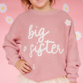 Sweet Wink Big Sister Knit Sweater
Child wearing a pink 'big sister' sweater against a pink background with daisies.