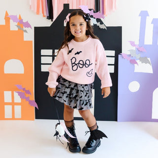 Sweet Wink Flocked Bats Halloween Bow Tiered Tutu 
Child wearing a pink 'Boo' sweater with Halloween-themed accessories in front of colorful cutout houses.