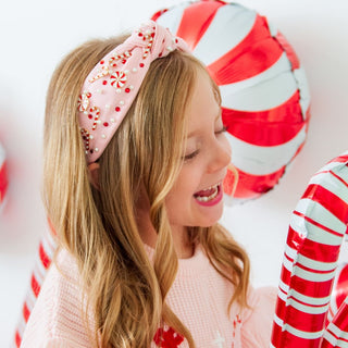 Sweet Wink Candy Cane Christmas Gemstone Headband - Kids
Young girl wearing a pink headband with candy cane decorations, smiling in front of candy cane-themed balloons.