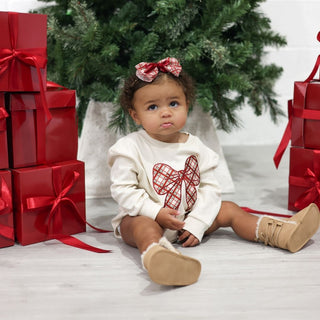Sweet Wink Christmas Plaid Bow Patch Long Sleeve Romper - Natural
Child in a white outfit with a red bow sitting among Christmas presents and a tree.