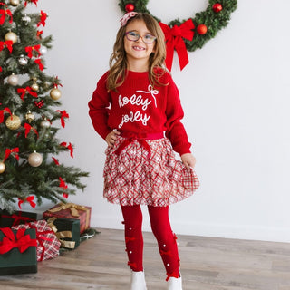 Sweet Wink Christmas Plaid Bow Tiered Tutu
Child wearing a red sweater with 'holly jolly' text, standing in front of a decorated Christmas tree.