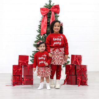 Sweet Wink Holly Jolly Bow Christmas Knit Sweater - Kids
Two children in matching red Christmas outfits standing in front of a decorated Christmas tree with red bows.