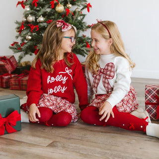 Sweet Wink Christmas Plaid Bow Patch Sweatshirt - Natural
Two young girls in festive outfits sitting in front of a Christmas tree with presents.
