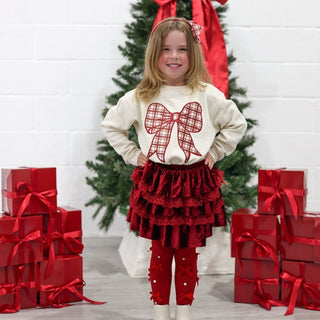 Sweet Wink Christmas Plaid Bow Patch Sweatshirt - Natural
Young girl in festive outfit with red bow and presents in front of a Christmas tree.