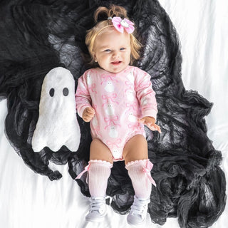 Baby in a pink ghost-themed outfit with a white ghost toy on a dark background