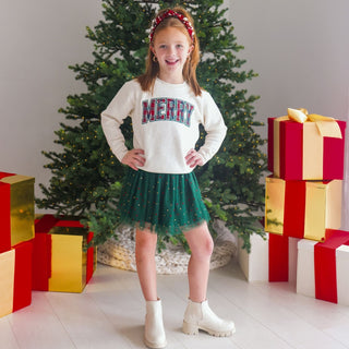 Model wearing Sweet Wink Merry Tartan Patch Christmas sweatshirt with a pearl headband, featuring festive tartan and holiday design.