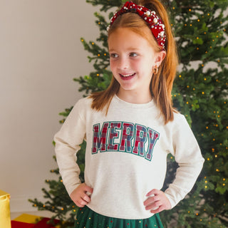 Model wearing Sweet Wink Merry Tartan Patch Christmas sweatshirt with emerald rhinestones and a pearl headband, festive holiday style.