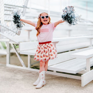 Sweet Wink Cheer Pearl Patch Short Sleeve T-Shirt - Ballet Young girl in a pink top and floral skirt with pom-poms on a white deck.
