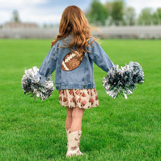 Sweet Wink Game Day Football Sequin Patch Denim Jacket Child in denim jacket with football design, holding pom-poms on a grassy field.
