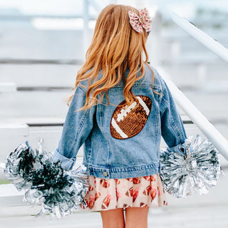 Sweet Wink Game Day Football Sequin Patch Denim Jacket Person wearing a denim jacket with a football patch, holding pom-poms, standing on a staircase.