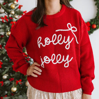 Sweet Wink Holly Jolly Bow Christmas Knit Sweater - Women's
Person wearing a red sweater with 'holly jolly' text in front of a decorated Christmas tree.