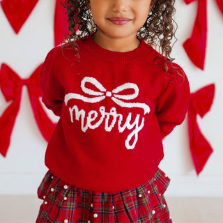 Model wearing Sweet Wink Merry Bow Christmas Sweater with festive design, paired with a tartan pearl skirt.