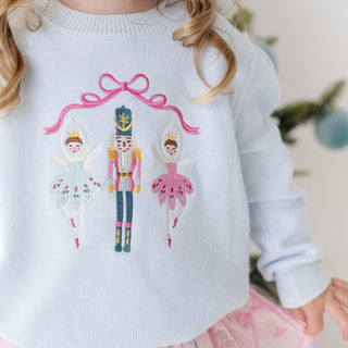 Model wearing Sweet Wink embroidered Christmas sweater featuring a nutcracker and festive holiday designs.