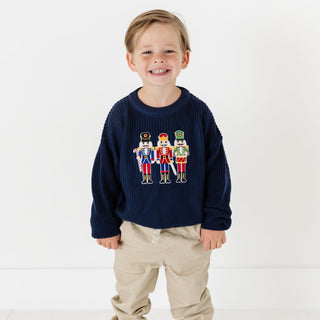 Model wearing Sweet Wink Nutcracker Patch Christmas sweater in khaki, featuring festive nutcracker design on a cozy knit fabric.