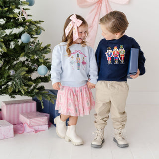 Model wearing a Sweet Wink Nutcracker Trellis Christmas Tutu Skirt, showcasing festive red and green fabric with decorative nutcracker motifs.