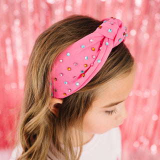 Sweet Wink Raspberry Rhinestone Headband
Child wearing a pink headband with colorful stones against a pink glittery background