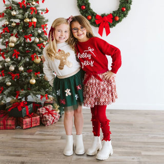 Sweet Wink Holly Jolly Bow Christmas Knit Sweater - Kids
Two children in festive outfits standing in front of a decorated Christmas tree and wreath.